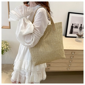 Detail of hand-woven straw tote bag featuring premium light brown leather shoulder straps