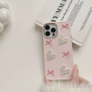 Pink iPhone 16 Pro Max case with 3D ribbons and heart charms in a lifestyle setting