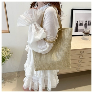Close-up of a large woven straw tote bag with brown leather straps on a model