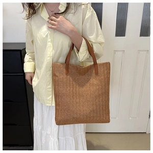 Detail of caramel straw woven tote bag showing herringbone pattern and leather handles