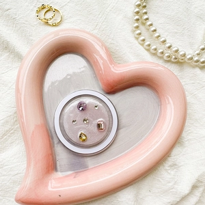Pink ceramic heart tray displaying colorful rhinestones and jewelry accessories
