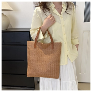 Detail of a large straw tote bag with brown faux leather handles and woven texture