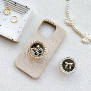 Detail of lychee pattern leather phone case with pearl-trimmed bow grip on stone tray