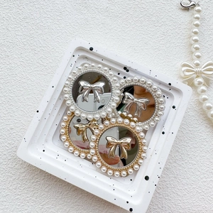 Close-up of gold and silver bow phone grips with pearl borders on a white tray