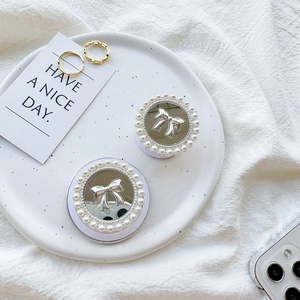 Top view of two pearl-rimmed mirror phone grips with silver bows on a ceramic tray