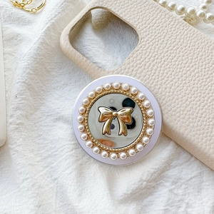 Detail of mirror phone grip with golden bow and pearl trim on white textured fabric