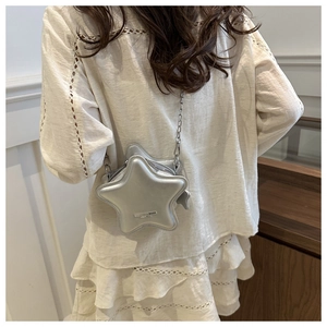 Detail of silver star-shaped crossbody bag with metal chain on white lace dress