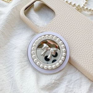 Detail of mirror phone grip with silver bow and pearls against soft fabric background