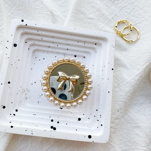 Macro shot of mirror phone grip with golden bow and pearl inlay on marble base