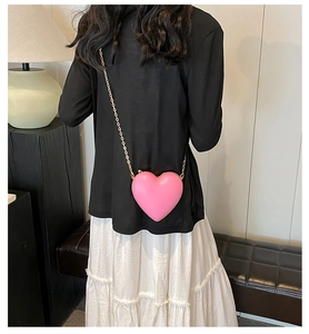 Model wearing a pink heart-shaped mini crossbody bag with gold chain over white skirt