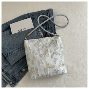 Detail shot of blue butterfly embroidery and golden metal hooks on white canvas bag