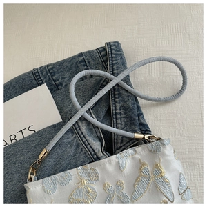 Detail of light blue satin bag featuring gold butterfly embroidery and metal lobster clasp