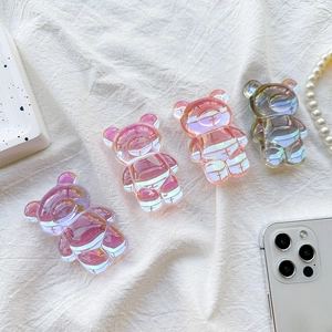 Macro detail of four iridescent bear-shaped phone grips on white fabric background