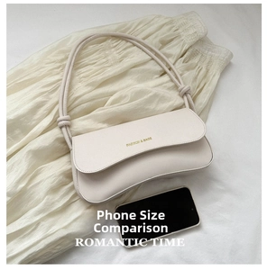 Chic beige shoulder bag detail with gold lettering shown next to a smartphone for scale