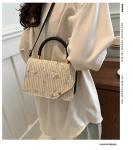 Detail of beige straw handbag with floral embroidery and black woven handle on model