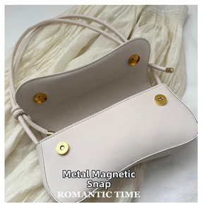 Detail view of cream shoulder bag with double magnetic hardware buckles and soft curved flap