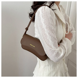 Detail of a brown leather shoulder bag with adjustable strap and knot decoration