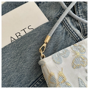 Macro detail of blue embroidery bucket bag featuring butterfly jacquard and gold metal hook