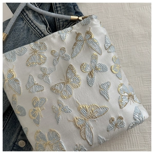 Detailed embroidery of blue and gold butterflies on a white satin bucket shoulder bag