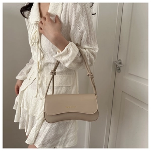 Close-up of beige faux leather shoulder bag with knotted strap and gold foil logo
