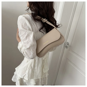 Detail of beige leather underarm bag featuring knotted strap and golden fashion text