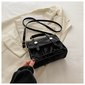 Détail d'un sac noir brillant à texture marbrée avec boucles dorées sur blazer