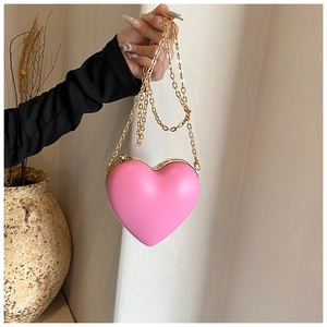 Detail of pink heart-shaped hard shell evening bag with gold chain strap held by model