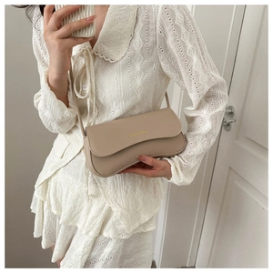 Detail of a minimalist cream crossbody bag with gold lettering held by a model in lace dress