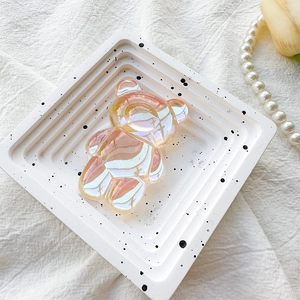 Detailed view of iridescent laser bear phone grip on textured white display tray