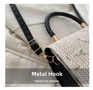 Close-up of golden hardware hooks and floral embroidery on a beige woven handbag