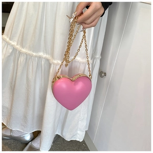 Pink heart-shaped crossbody bag with gold chain strap shown on white dress