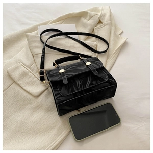 Détail d'un sac à main noir marbré avec boucle dorée et téléphone pour comparer la taille