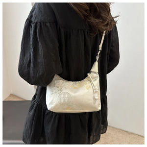 Detail of a beige satin bucket bag with traditional floral embroidery and beaded pendant
