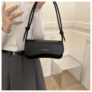 Detail of black faux leather shoulder bag with gold text and decorative knotted strap