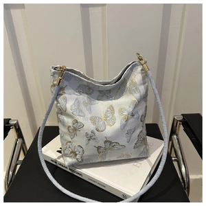 Macro detail of golden butterfly embroidery on light blue canvas shoulder bag with metallic hook