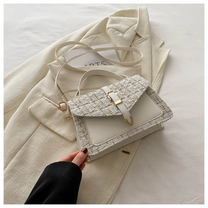 Détail d'un sac en tweed et cuir blanc avec fermoir doré posé sur une veste de blazer
