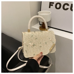 Detail of woven straw bag showing delicate floral embroidery and textured braided handle