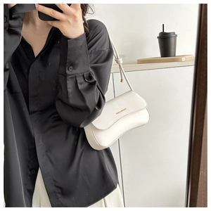 Close-up of a stylish off-white underarm bag with gold lettering and a knotted strap detail