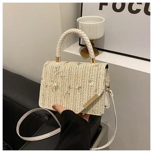 Detail of woven straw handbag featuring delicate floral embroidery and gold metal clasp