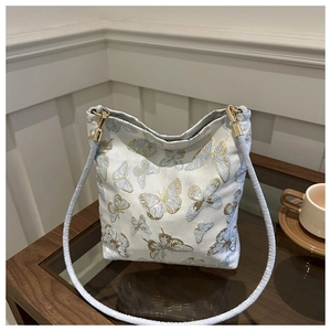Detailed embroidery of gold and blue butterflies on a canvas bucket bag with gold hardware