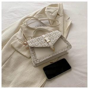Détail du sac en tweed et cuir crème avec boucle dorée posé sur un blazer beige