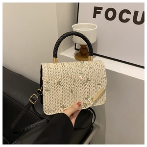 Detail of hand-woven beige straw bag with delicate floral embroidery and black handles