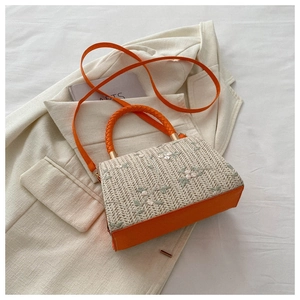 Detailed close-up of straw woven bag with floral embroidery and orange leather handles