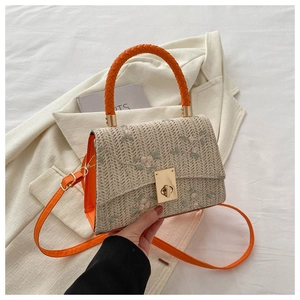 Detail of straw woven bag with floral embroidery, orange leather trim and golden clasp
