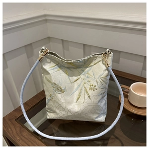 Detail of embroidered bamboo and birds on cream-white fabric bucket bag with metal hooks