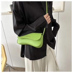 Detail of neon green curved crossbody bag with wavy flap shown on a model's outfit