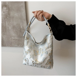 Detailed close-up of blue butterfly embroidery and golden metal rings on a fabric handbag