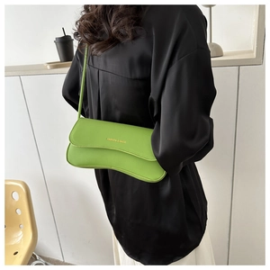 Close-up of grass green crossbody baguette bag with gold lettering on a model