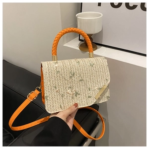 Detailed embroidery of flowers on a woven straw bag with orange textured strap