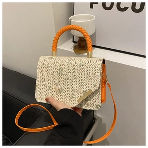 Detail of straw woven handbag featuring floral embroidery and orange handle in hand